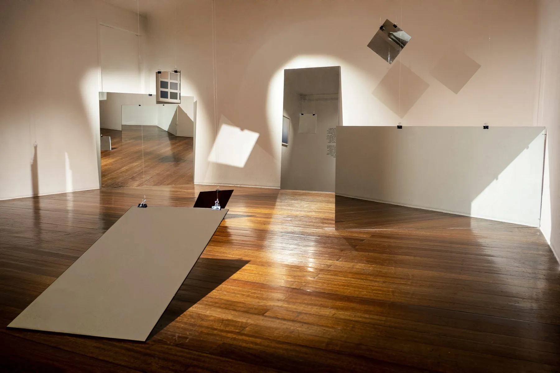 A room of hanging and leaning mirrors and panels casting light and shadow on a wooden floor