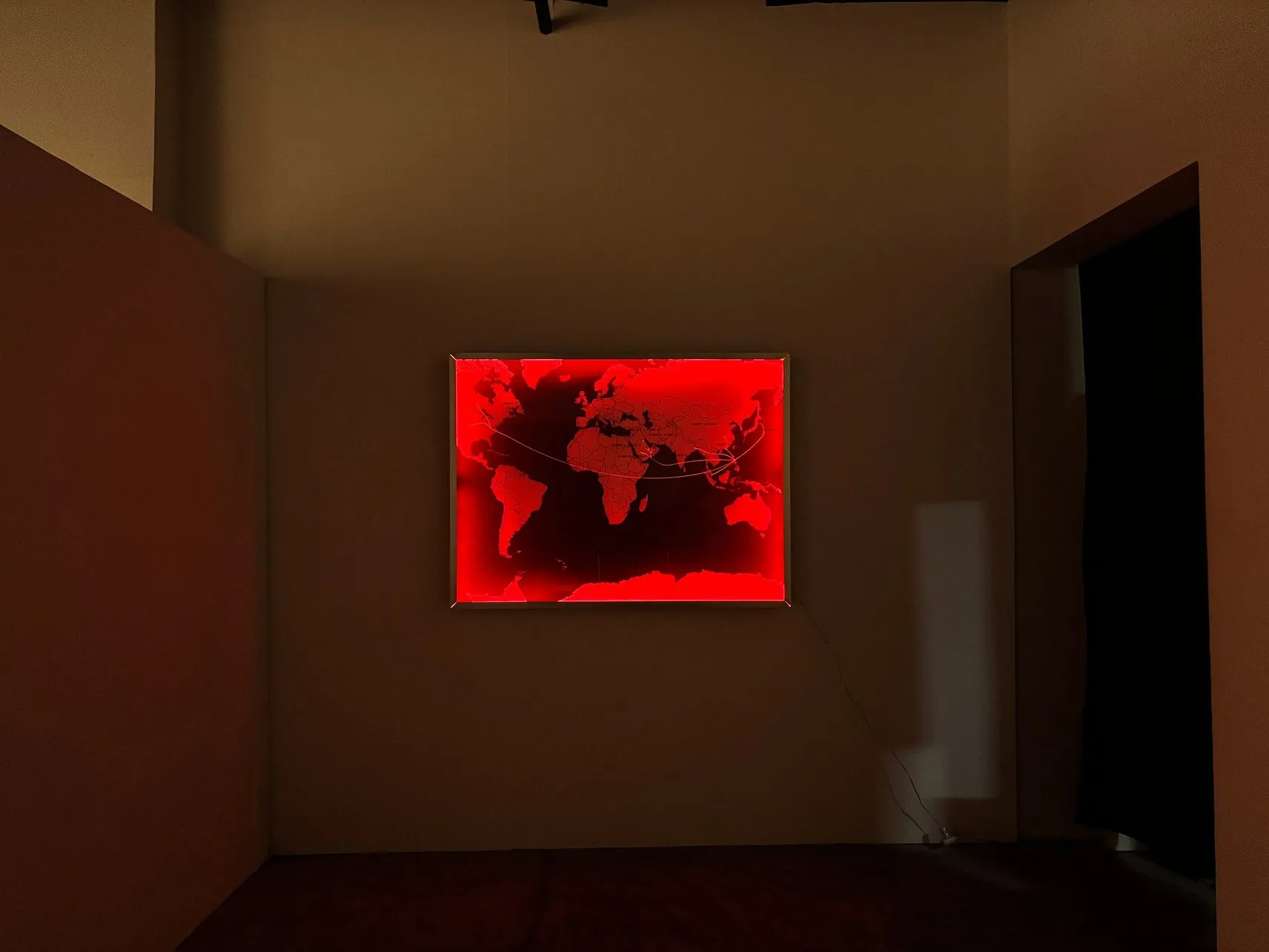 A world map in red-lit acrylic glass hanging in a dark gallery