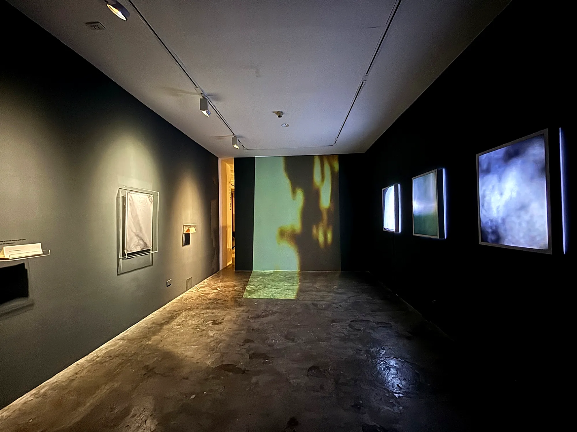 Dark gallery with backlit prints, a projection and works in acrylic glass