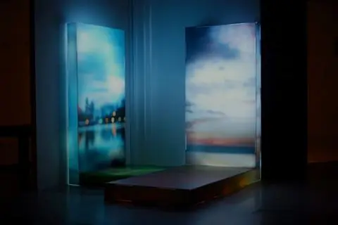 Two tall glowing acrylic panels printed with sunsets, set at an angle in a dark corner