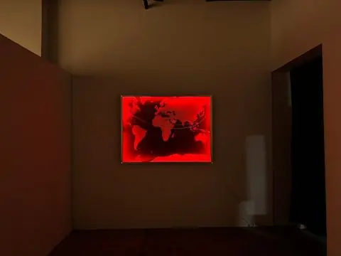 A world map in red-lit acrylic glass hanging in a dark gallery